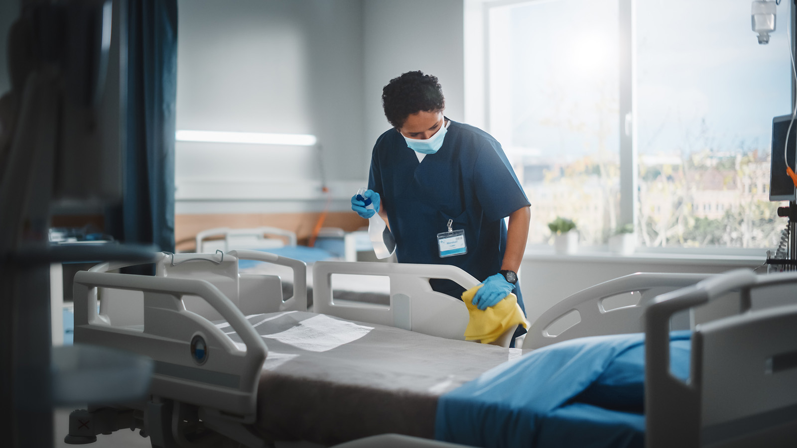 A janitorial employee is disinfecting a hospital bed